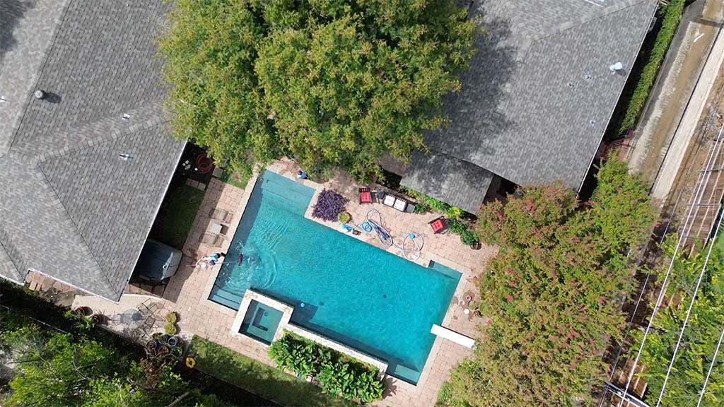 Aerial view of a backyard with a large pool, surrounding patio, and trees.